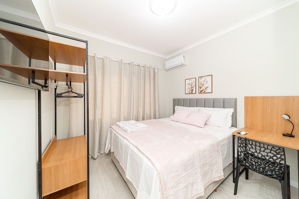 Quarto com cama, escrivaninha, cadeira, guarda-roupa e ar condicionado.