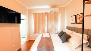 Une chambre à coucher avec un lit, des rideaux, un téléviseur à écran plat et des œuvres d’art accrochées au mur.