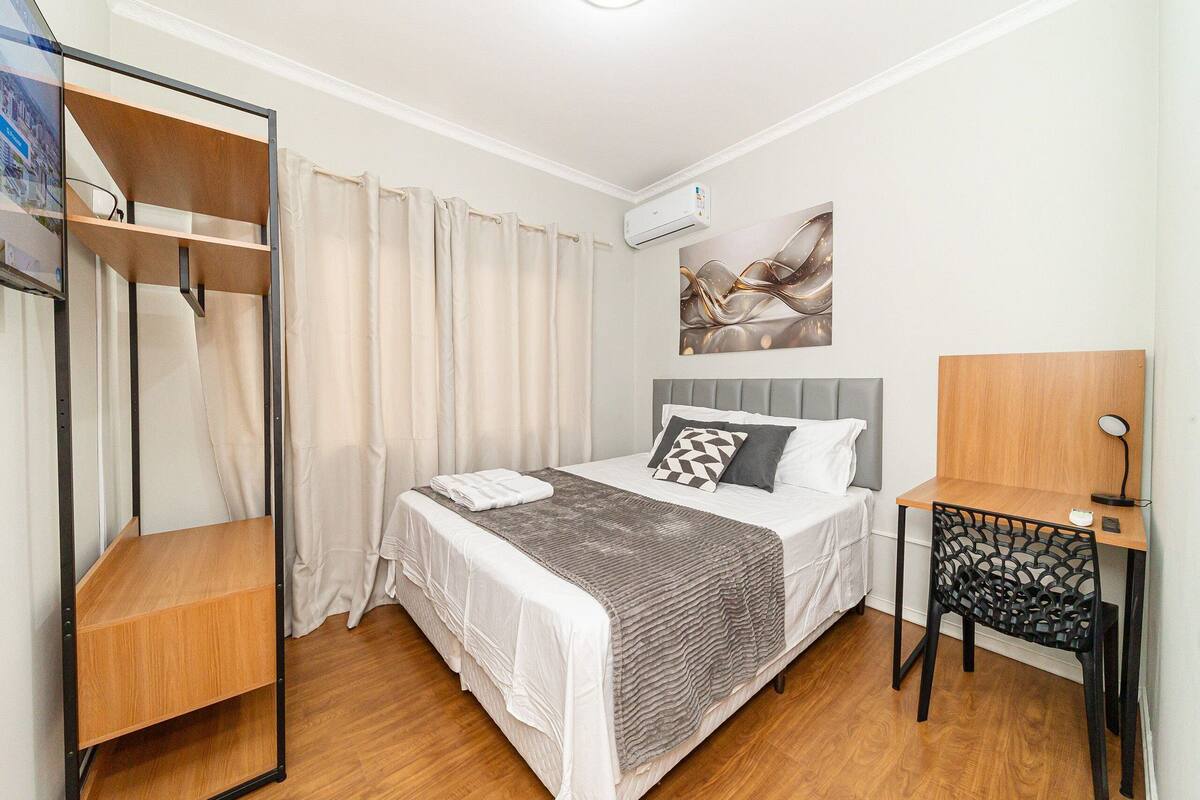 Quarto com cama, escrivaninha, cadeira, guarda-roupa e ar condicionado.