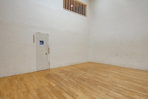 Een kamer met een houten vloer, een witte deur met een klein raam, en een gevlinderd raam erboven.