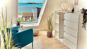 A room with a large window, a blue chair, a white cabinet, and several potted plants. - Ferienwohnung in Orth auf Fehmarn (Fehmarn)