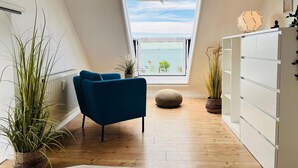 A room with a skylight, a blue chair, wooden flooring, and a white cabinet. - Ferienwohnung in Orth auf Fehmarn (Fehmarn)