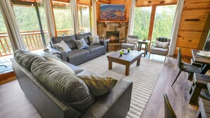 Een gezellig interieur van een chalet met een open haard, een bank, een eettafel en uitzicht op het bos.