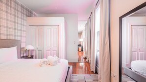 Ein Hotelzimmer mit einem großen Bett, einem Nachttisch mit Lampe, einem Kleiderschrank und einem Flur, der in einen anderen Raum führt.