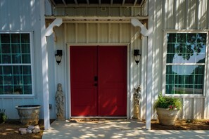A red door with a white porch and two wall-mounted lights.