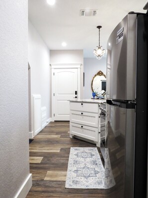 A kitchen with a refrigerator, a white door, a chandelier, and a patterned rug. - Delightful 1-bedroom barn with AC in charming Saint Jo (Saint Jo)