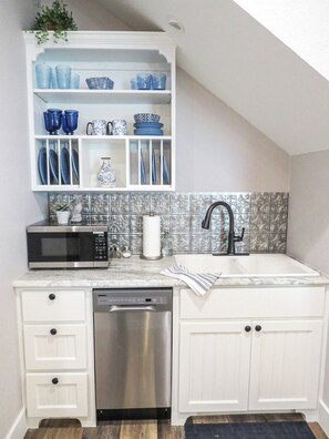 A kitchen with white cabinets, a stainless steel dishwasher, a microwave, and a sink with a black faucet.