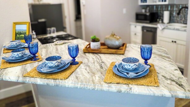 A kitchen with a marble countertop, blue glassware, and a framed picture on the wall. - Saint Jo Wine Country Barn - Walk to Blue Ostrich Winery (Saint Jo)