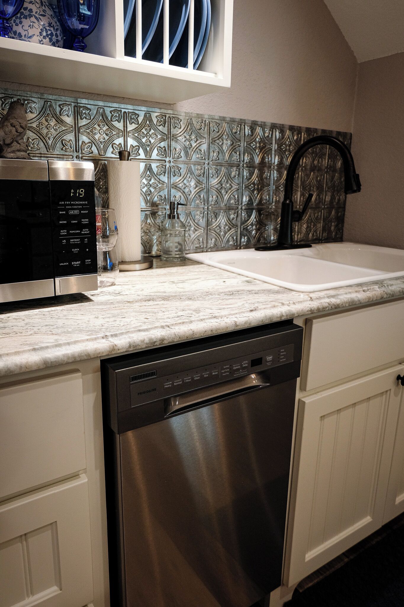 A kitchen with a dishwasher, a microwave, a sink, and a decorative backsplash.