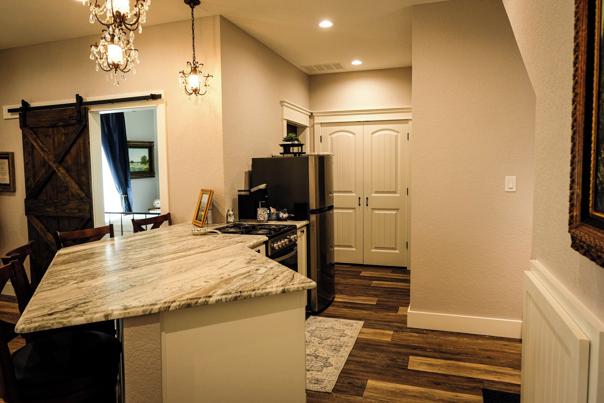 A kitchen with a marble countertop, a refrigerator, a stove, and a chandelier.