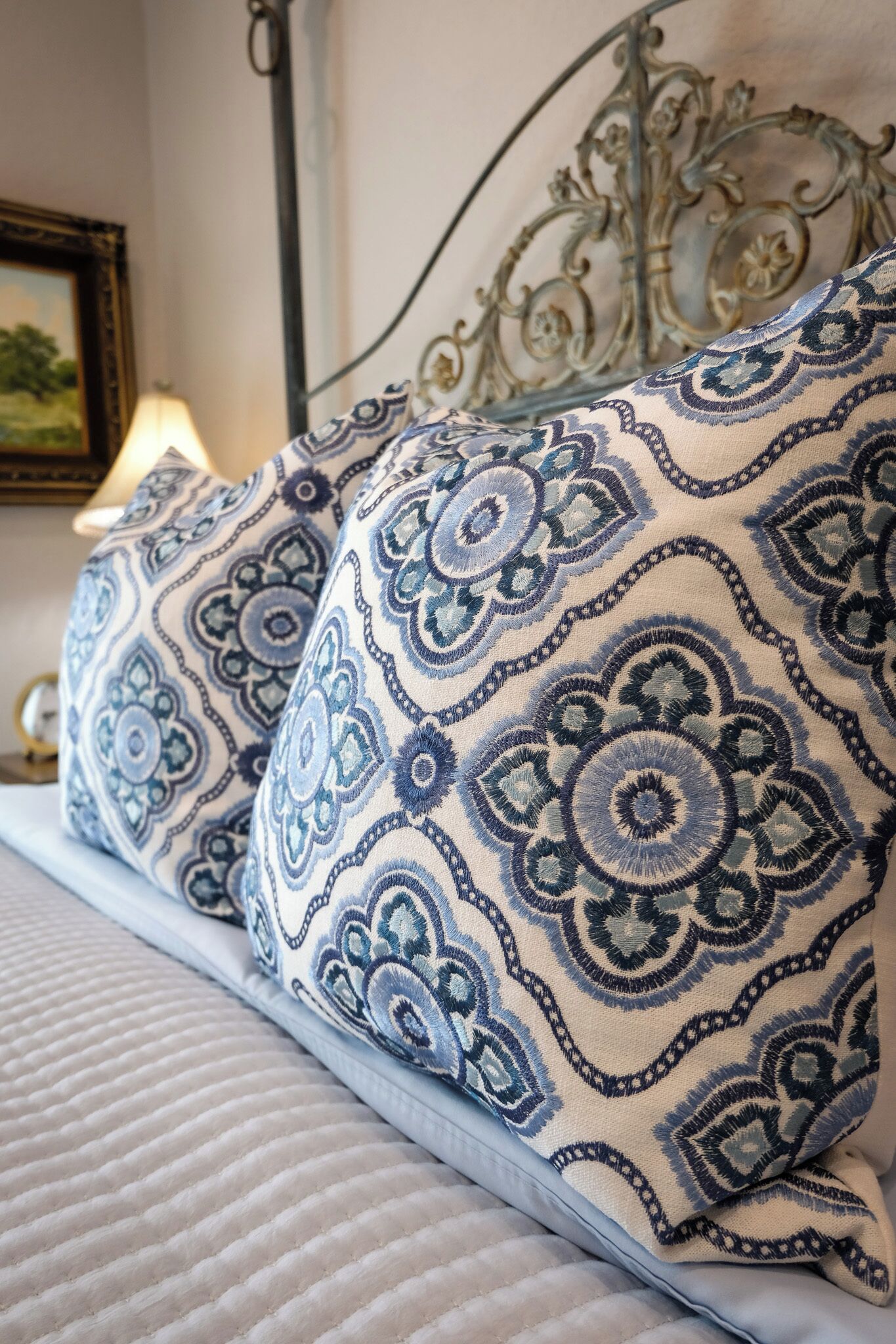 A bed with patterned pillows, a metal headboard, and a lamp in the background.
