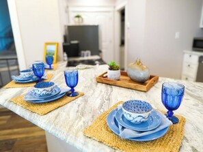 A kitchen counter with blue glassware and plates, a wooden tray with a plant, and a marble countertop.