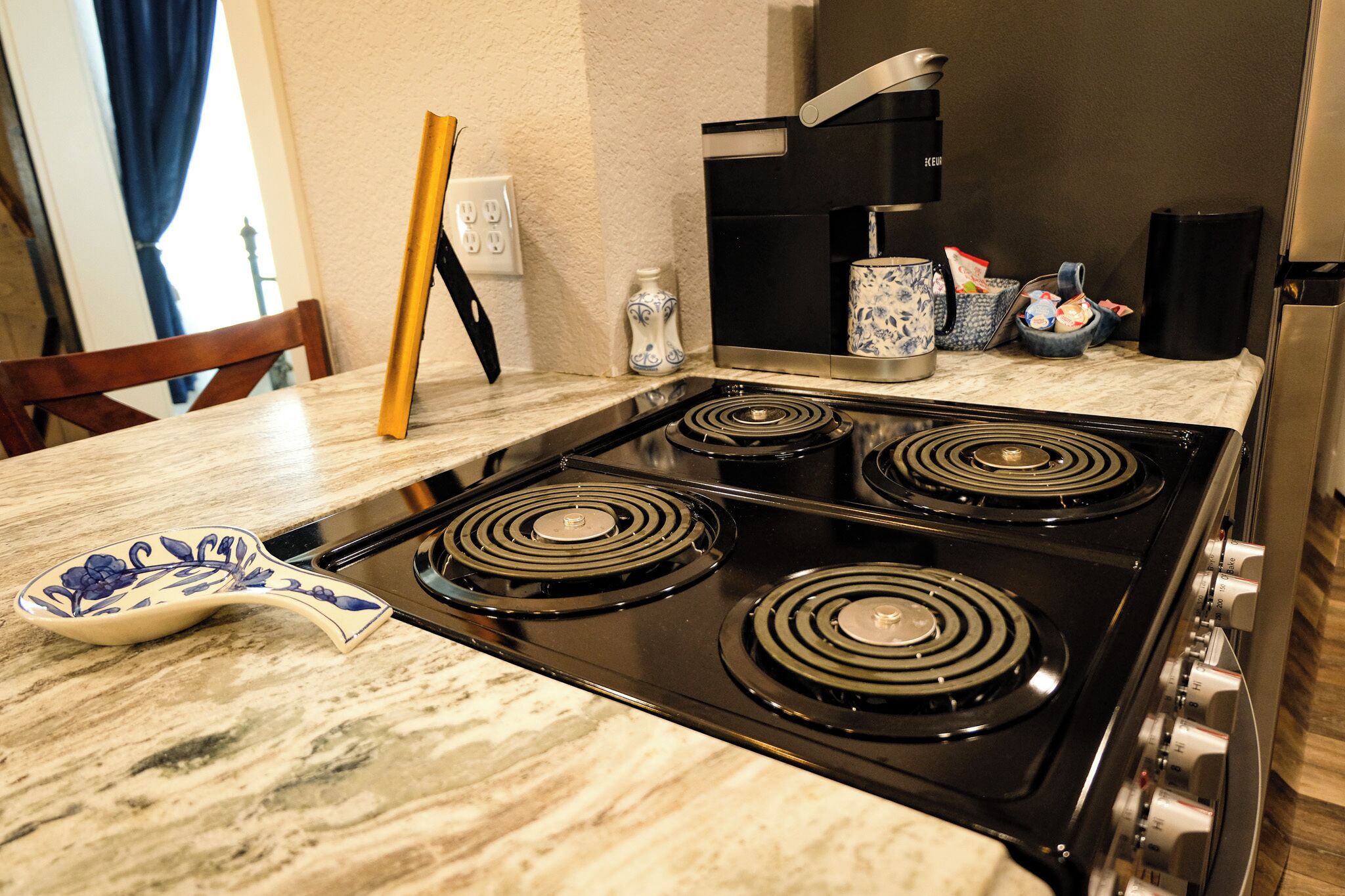 A kitchen with a four-burner stove, a marble countertop, and a coffee maker.