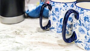 A coffee maker, two blue floral mugs, and a power outlet on a countertop. - Saint Jo Wine Country Barn - Walk to Blue Ostrich Winery (Saint Jo)