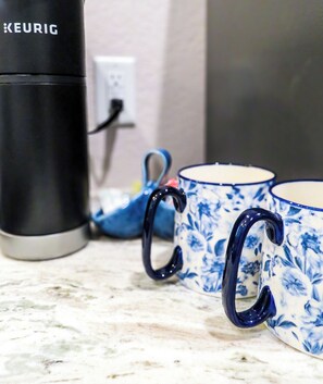 A coffee maker, two blue floral mugs, and a power outlet on a countertop.