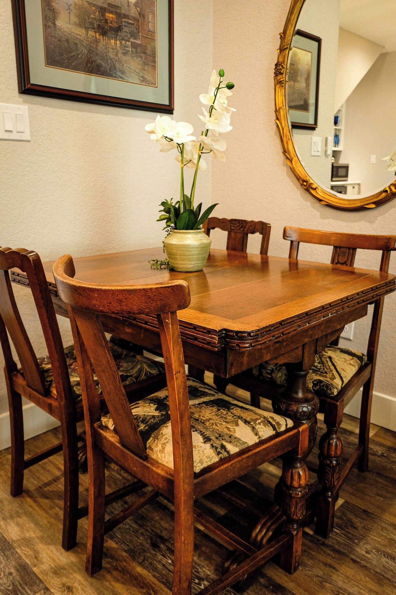 Een eettafel met stoelen, een vaas met bloemen en een spiegel aan de muur.