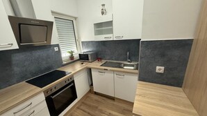 Cozinha compacta com micro-ondas, forno, pia e janela com persianas.