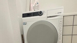 Máquina de lavar e secar empilhadas, com painel de controle, reservatório de água e parede revestida com azulejos.
