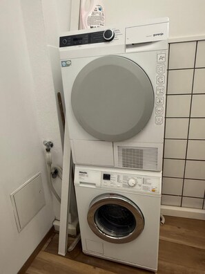A stacked washer and dryer unit with a control panel, a water tank, and a tiled wall. - Hüttenberg vacation home (Hüttenberg)