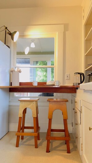 A kitchen with a window, two wooden stools, a countertop, and a kettle.