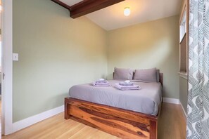 A bedroom with a wooden bed frame, a single bed with two pillows, and a light-colored wall.