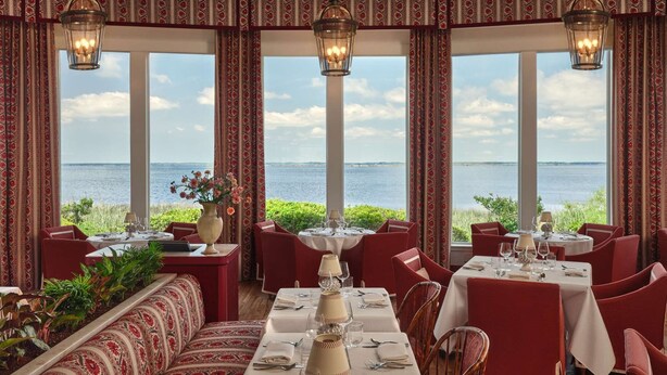 A restaurant with tables set for dining, large windows with a view of the sea, and patterned curtains. - King Suite on the Outer Banks + Restaurants & Spa (Duck)