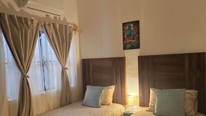Quarto de hotel com duas camas, um ventilador de teto, aparelho de ar condicionado e um quadro na parede.