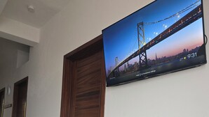 Um corredor com porta de madeira, piso ladrilhado e uma TV na parede exibindo uma vista urbana.