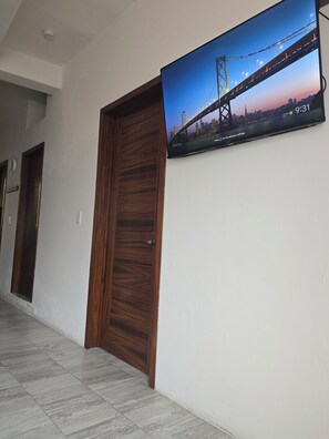 Ein Flur mit Holztür, gefliestem Boden und einem an der Wand befestigten Fernseher, der eine Stadtansicht zeigt.