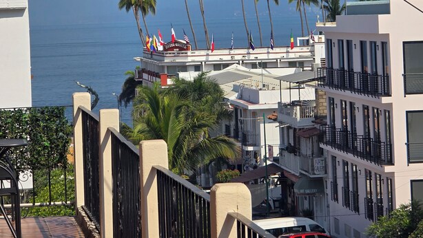 Um hotel com vista para o mar, palmeiras e uma varanda com guarda-corpo.