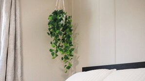 Uma cama com duas almofadas, uma planta pendurada e uma cortina.