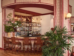 Eine Bar mit einer hohen Theke, mehreren Pendelleuchten und einer Auswahl an Flaschen und Gläsern auf Regalen.