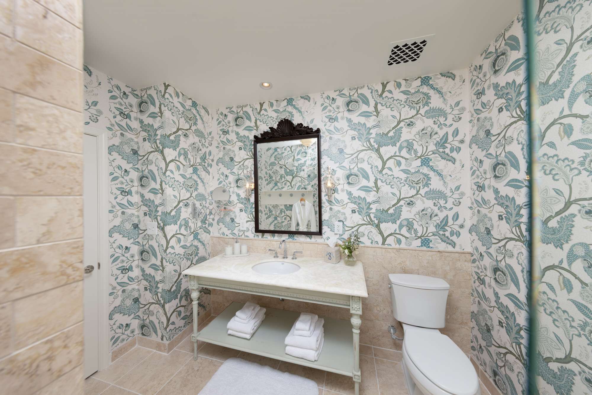 Casa de banho com papel de parede floral, um lavatório, uma sanita e um espelho.