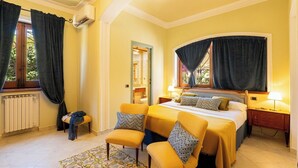 A hotel room with a bed, two chairs, a nightstand, a lamp, a window with curtains, and a radiator. - Seaside villa, suitable for families and friends, only 5 minutes from the Valley of the Temples. (San Leone)