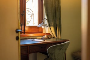 A desk with a lamp, a chair, a window with curtains, and a door.