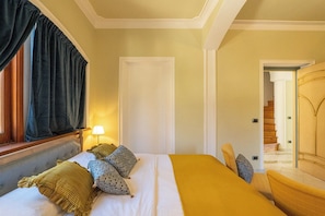 A hotel room with a bed, a lamp, a chair, and a door leading to a staircase.