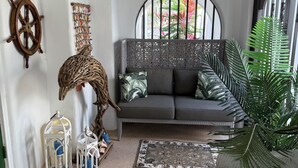 Une pièce chaleureuse avec un canapé gris, un fauteuil en osier, des lanternes décoratives et un gouvernail de bateau accroché au mur.