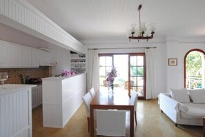 A dining area with a wooden table and chairs, a white sofa, and a kitchen area with white cabinets. - Superior Apartment with Sea Views & Sunset Veranda at Stavento Apartments (Argostolion)