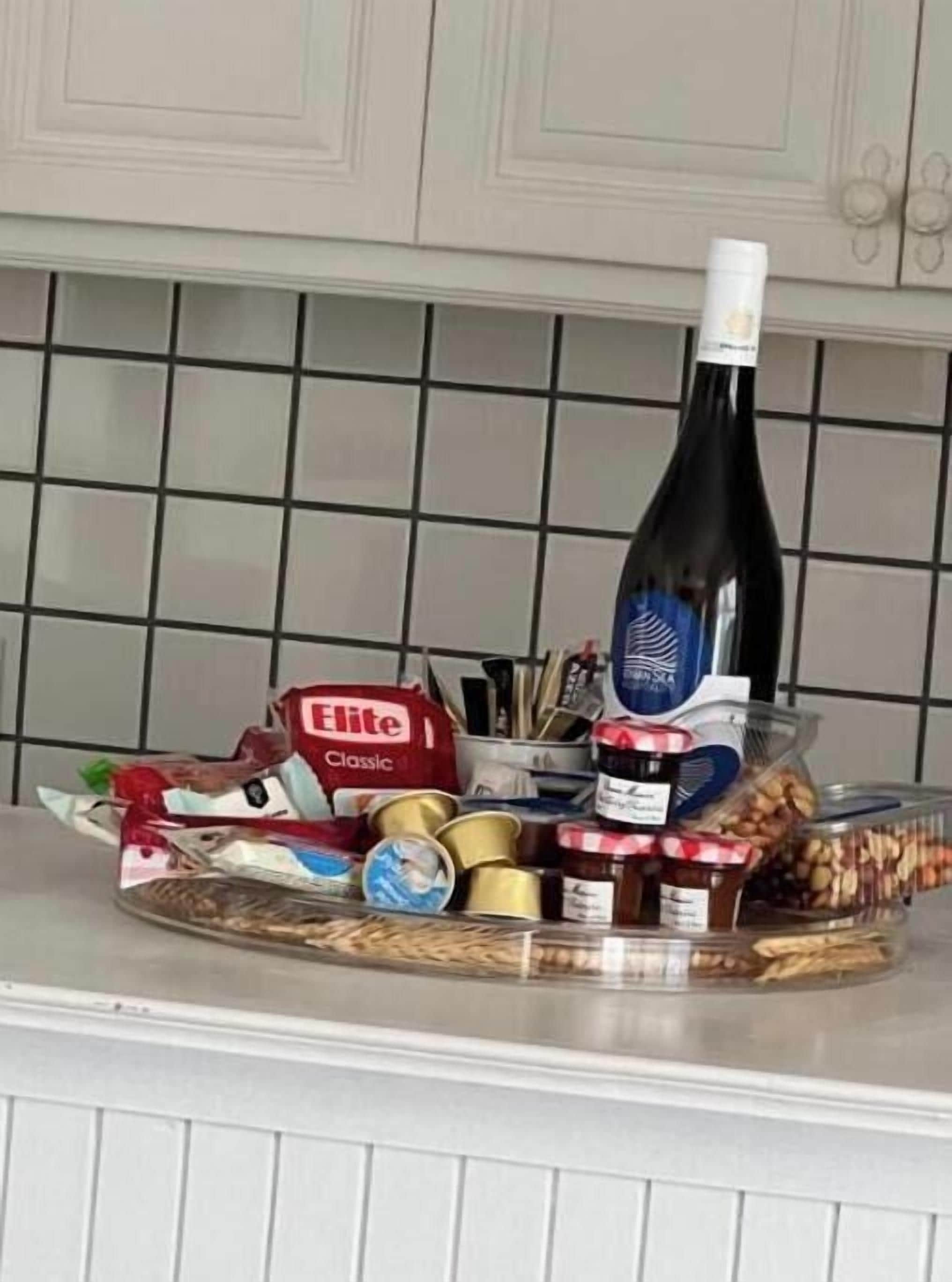 A kitchen counter with a bottle of wine, a jar of jam, a container of nuts, and a bag of chips.