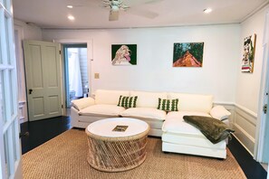 A living room with a white sofa, a round wicker coffee table, and two paintings on the wall. - The Walcott Cottage: Walkable Historic Retreat in Thomasville (Thomasville)