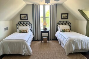 Una habitación con dos camas, una mesita de noche con una lámpara y una ventana con cortinas.