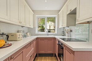 Eine moderne Küche mit weißen Schränken, einem Fenster mit Blick auf Grünflächen, einem Toaster und einer Spüle.