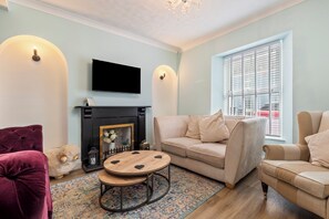 Ein Wohnzimmer mit Kamin, einer Couch, einem Sessel, einem Fernseher und einem gemusterten Teppich.