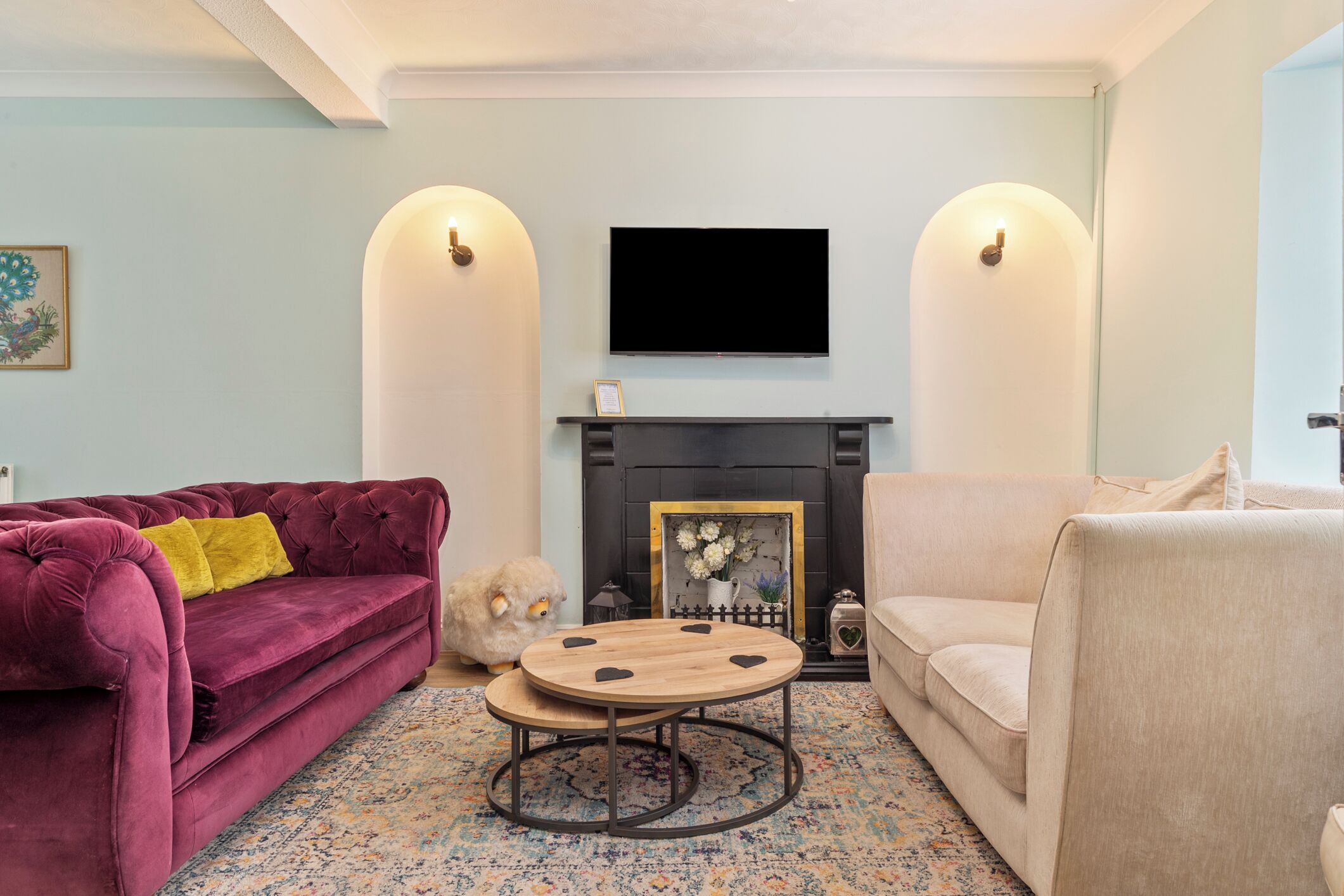 Una sala de estar con chimenea, un televisor montado encima, un sofá rojo y mullido, un sillón color beige y una mesa de centro redonda de madera.