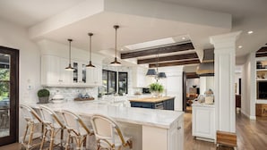 A spacious kitchen with white cabinetry, a large island, and three wicker bar stools. - Gated 7BR Rancho Santa Fe Estate Pool/Guest House (Rancho Santa Fe)