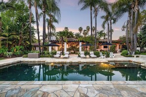 A pool area with lounge chairs, umbrellas, and a building with a tiled roof.