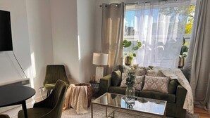 Ein Wohnzimmer mit einer Couch, einem Couchtisch, einem Sessel, einer Lampe und einem Fernseher.