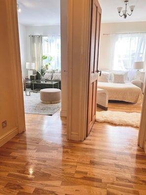 A room with a wooden floor, a bed with white bedding, a sofa, and a lamp. - Lovely 1Bdr flat next to Earl’s Court Station (Greater London)