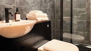 Ein modernes Badezimmer mit Marmorfliesenspiegel, Waschbecken, Toilette und einer Duschkabine aus Glas.