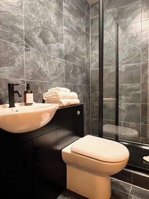A modern bathroom with a marble backsplash, a sink, a toilet, and a glass shower enclosure. - Lovely 1Bdr flat next to Earl’s Court Station (Greater London)